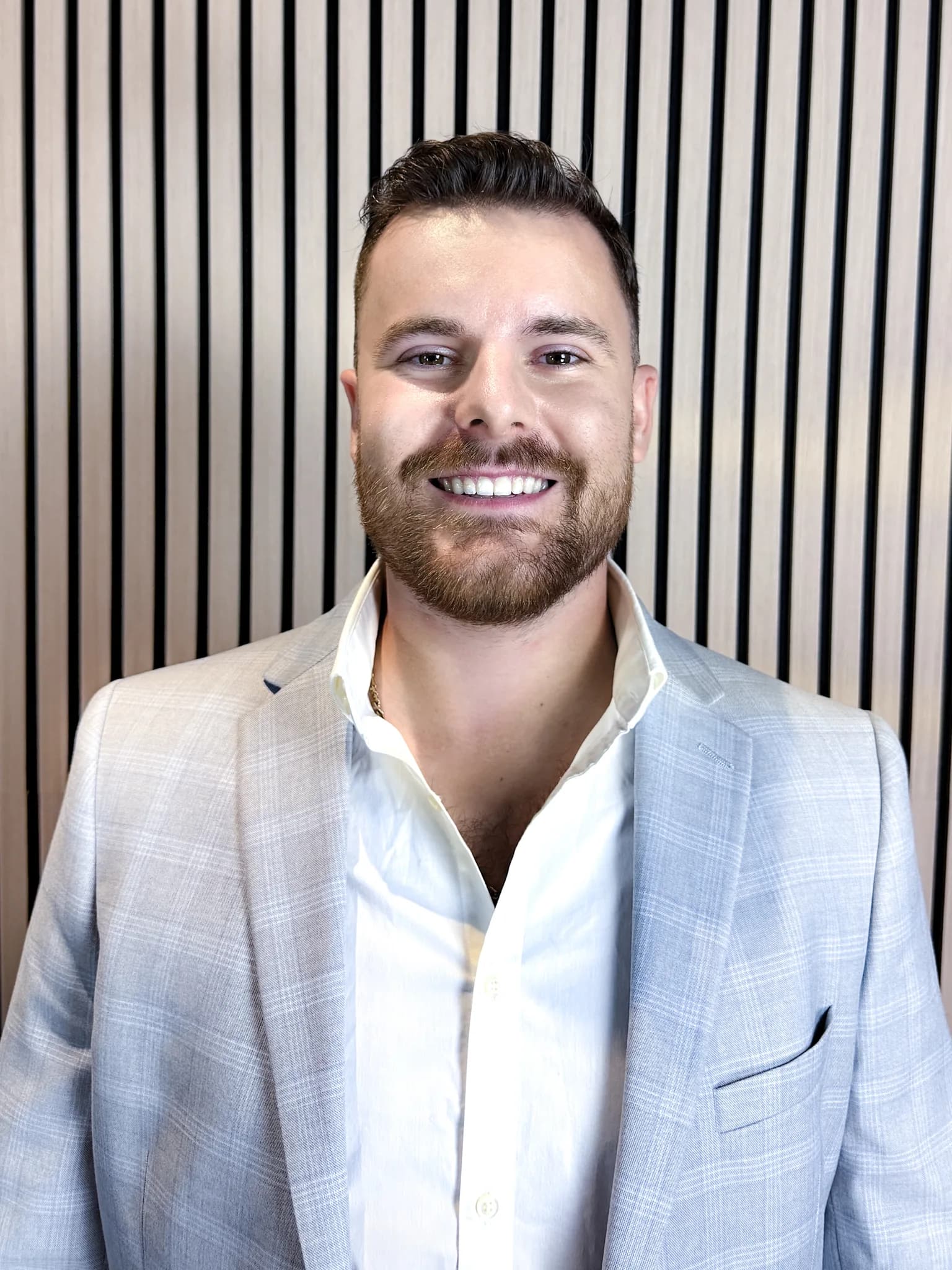 Portrait of Mason Arens, licensed advisor, smiling in a light blue checked blazer and open-collared white shirt
